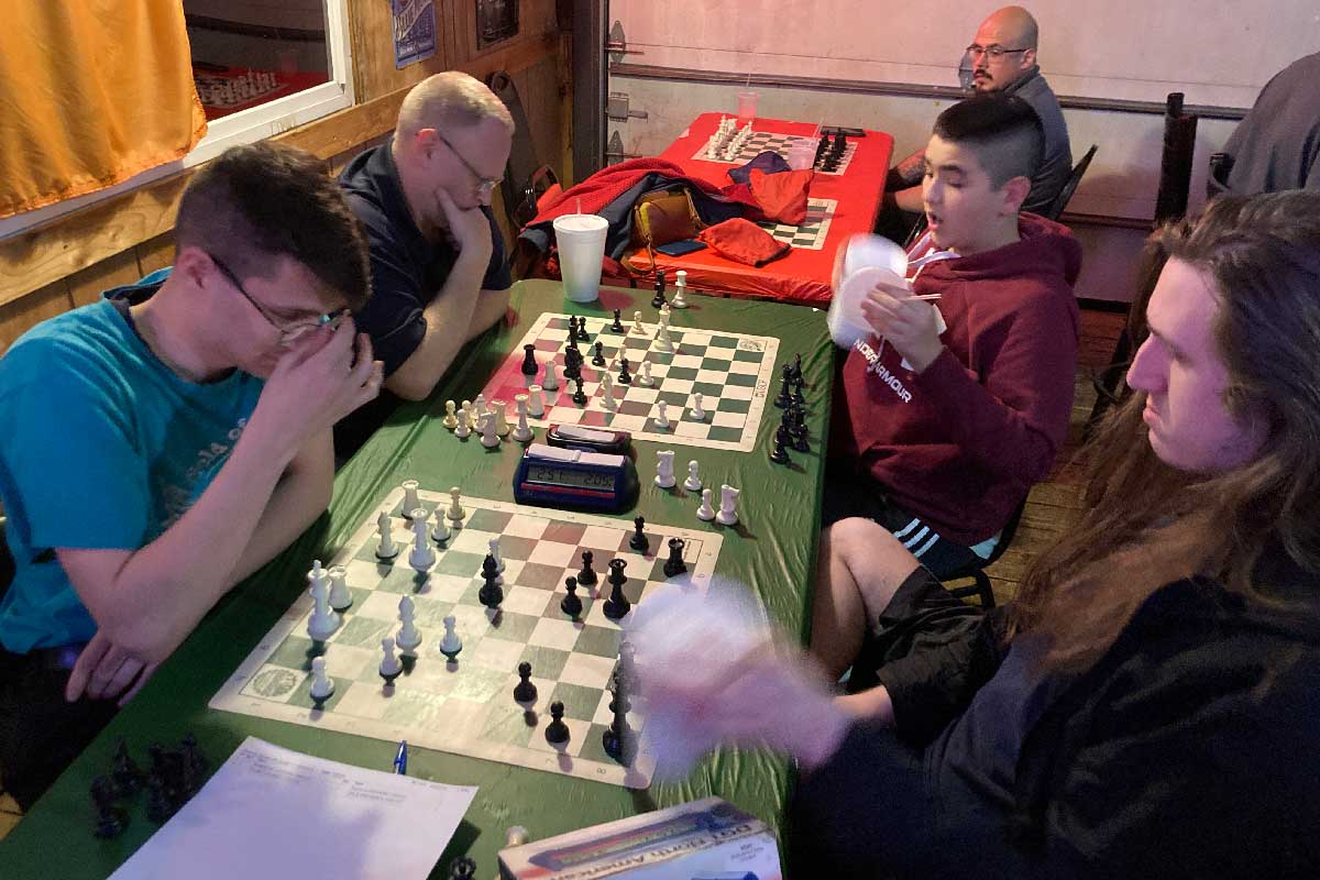 Four young men playing chess at Speedy Quads