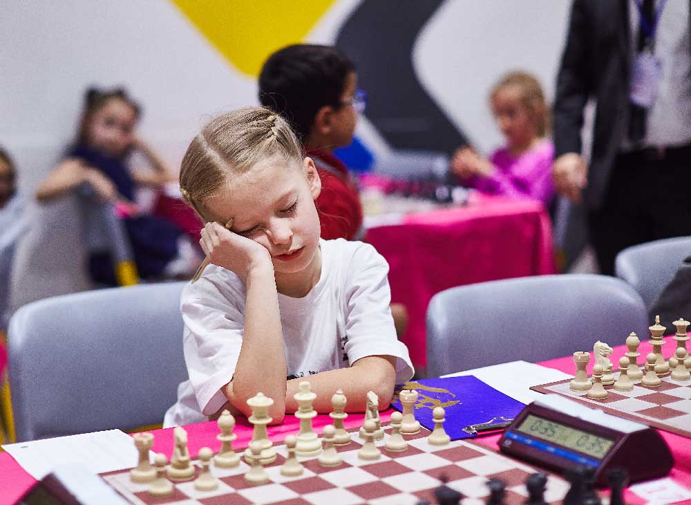 School-aged girl sitting at a chess board before a tournament game